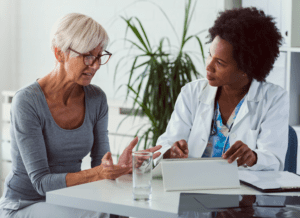 A female doctor sits at her desk and chats to an elderly female patient while looking at her test results